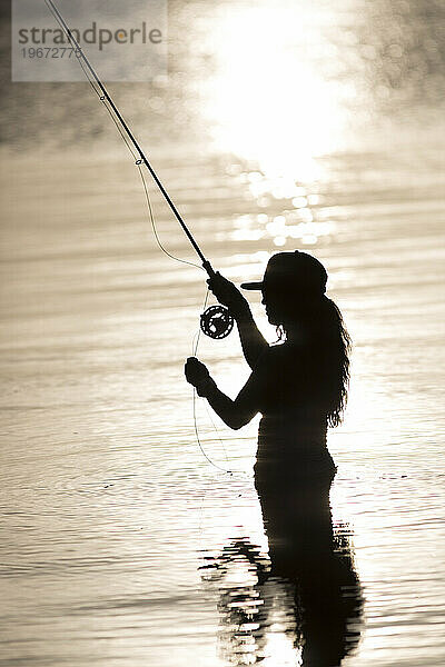 Silhouette einer Frau beim Fliegenfischen