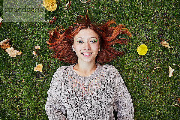 Lächelndes Mädchen mit roten Haaren  das auf grünem Gras liegt