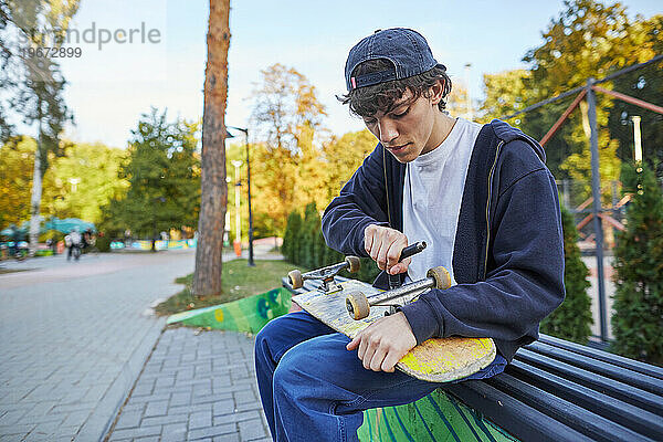 Skateboarder repariert seinen Skate im Park auf einer Bank