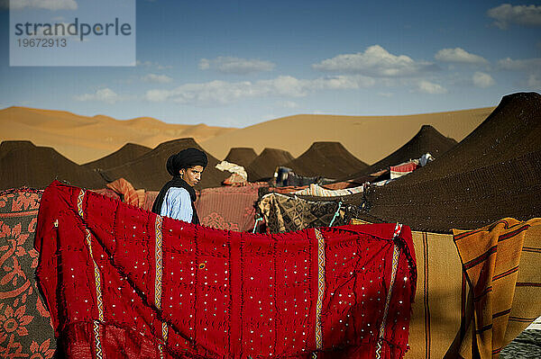 Ein Wüstenführer in traditioneller Kleidung geht durch ein Zeltlager mit bunten Decken.