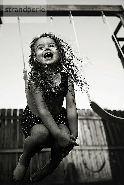 Schönes glückliches kleines Mädchen  das im Hinterhof schaukelt