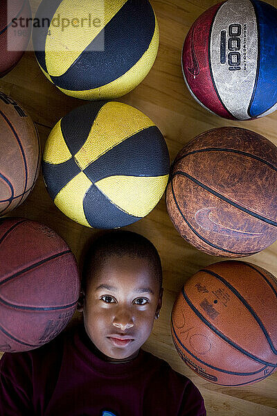 Ein kleiner Junge liegt inmitten einer Gruppe Basketbälle.