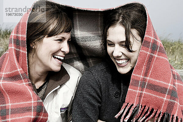 Zwei Freunde lachen gemeinsam unter einer Decke.