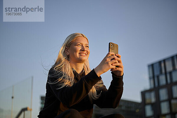 Glückliche Frau  die auf der Straße ein Foto mit dem Smartphone macht