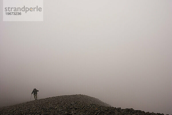 Ein einsamer Wanderer klettert durch den Nebel in der Nähe von Stony Dome im riesigen Hinterland des Denali-Nationalparks  Alaska.