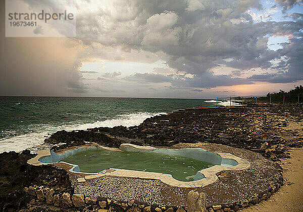 Ein dramatischer Himmel über einem kleinen Pool am Meer.