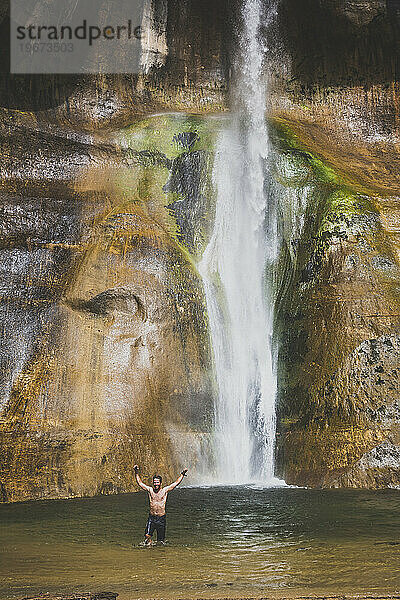 Ein Mann hält seine Arme hoch  nachdem er in einem Pool unter einem Wasserfall geschwommen ist.