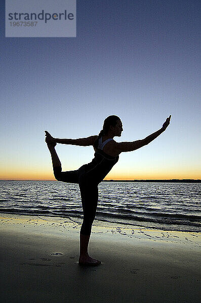 Die Silhouette einer Frau  die bei Sonnenuntergang am Strand auf Hilton Head Island  SC  Yoga macht.