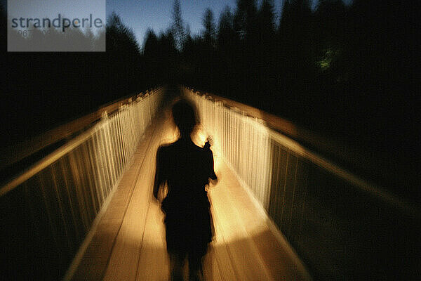 Die Silhouette einer Frau zeichnete sich im Licht ihrer Taschenlampe ab  als sie eine Fußgängerbrücke überquerte. (Bewegungsunschärfe)