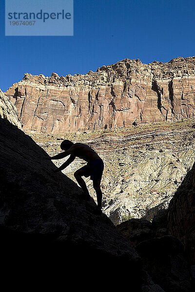 Ein silhouettierter Mann klettert eine Felswand im Eardley Canyon  San Rafael Swell  Utah  hinauf.