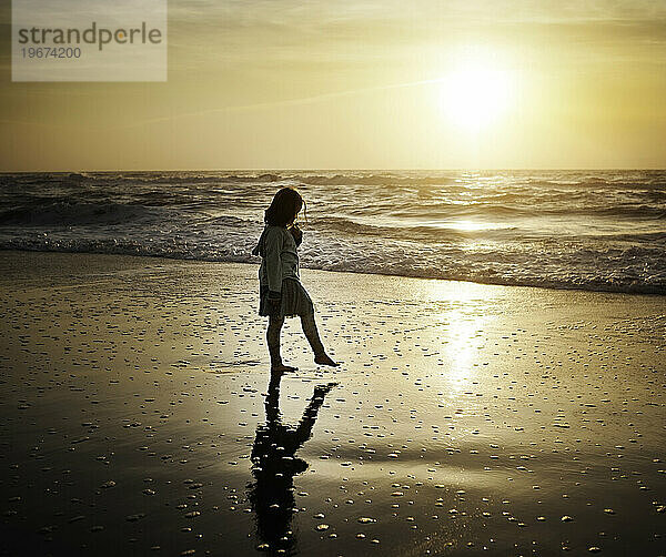 Junges Mädchen geht am Strand entlang und betrachtet das Spiegelbild bei Sonnenaufgang