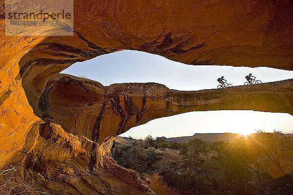 Ein Mann und eine Frau reiten über einen natürlichen Felsbogen in der Wüste in der Nähe von Moab  Utah.