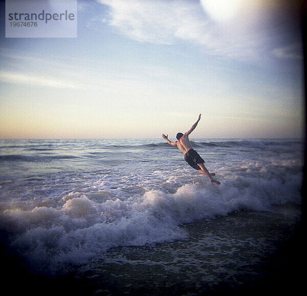 Ein junger Mann springt über eine tosende Welle. (Lochloch)