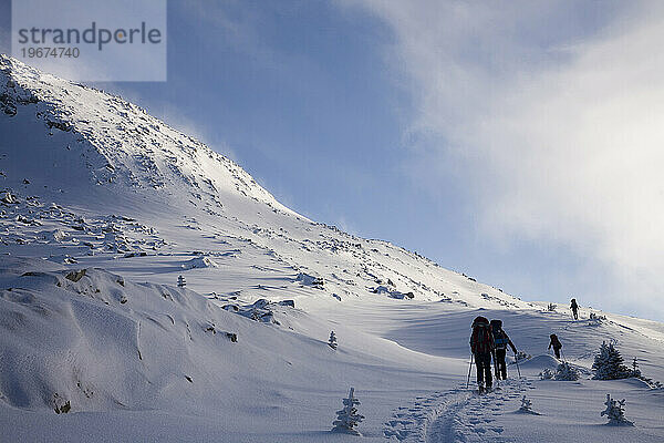 Silhouette zweier Backcountry-Skifahrer  die bei Sonnenaufgang einen Hang in den Bergen erklimmen.