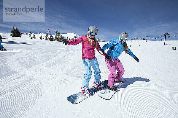 Zwei Snowboarderinnen haben Spaß daran  Snowboarden zu lernen.