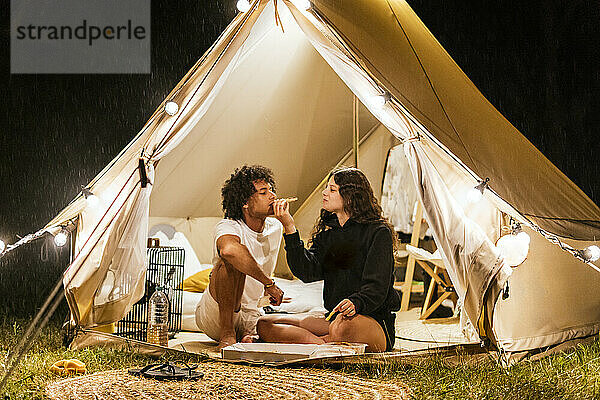 Verliebtes Paar isst Pizza in einem Campingzelt