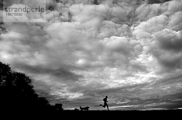Während atemberaubende Wolken den Himmel bedecken  laufen ein Mann und sein Hund über eine Wiese in der Nähe von Corvallis  Oregon.