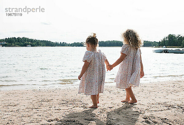 Händchenhaltende Schwestern gehen am Strand entlang zum Meer