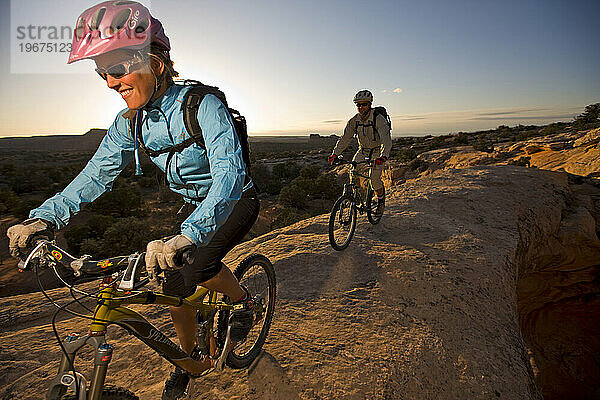 Ein Mann und eine Frau reiten über einen natürlichen Felsbogen in der Wüste in der Nähe von Moab  Utah.