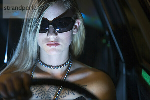 Vorderansicht einer jungen blonden Frau  die nachts mit Sonnenbrille fährt.