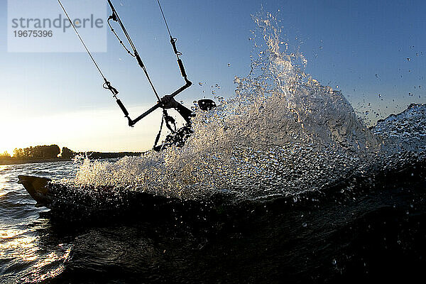 Tiefwinkelperspektive Silhouette eines Kiteboarders  der in den Sonnenuntergang schnitzt.