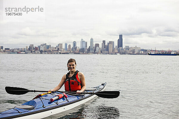 Ein junges Mädchen fährt an einem bewölkten Tag Kajak im Puget Sound vor der Küste der Innenstadt von Seattle.