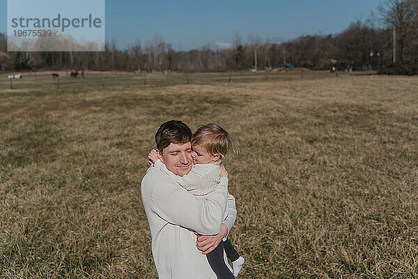 Ein Mann umarmt ein kleines Kind fest auf einem trockenen Feld