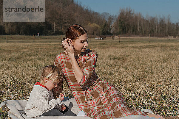 Rothaarige Frau mit Kind sitzt auf einem Plaid auf einem trockenen Feld