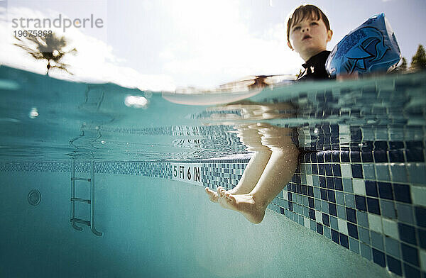 Split-Level-Junge am Beckenrand mit Beinen im Wasser