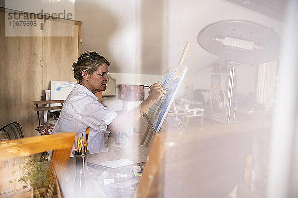 Innenansicht eines Ateliers mit einer älteren Frau  die ein Bild malt.