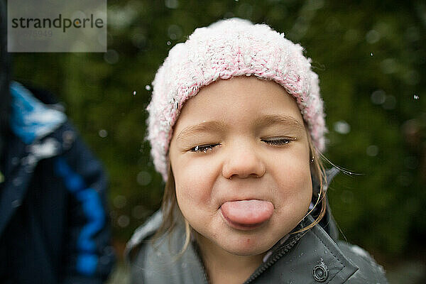 Junges Mädchen fängt draußen Schneeflocken mit der Zunge.