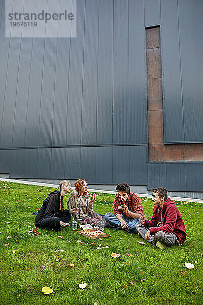 Studenten essen Pizza und lachen im Innenhof des Campus