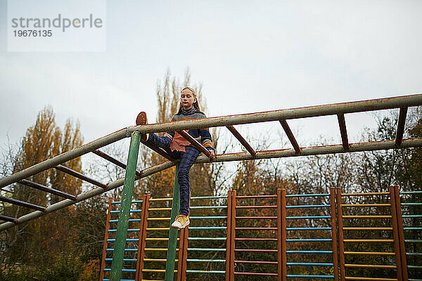 Ruhiges Teenager-Mädchen  das auf dem Klettergerüst am Spielplatz sitzt