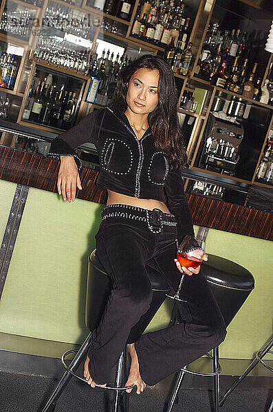 Eine Frau sitzt mit einem Drink an einer Bar.