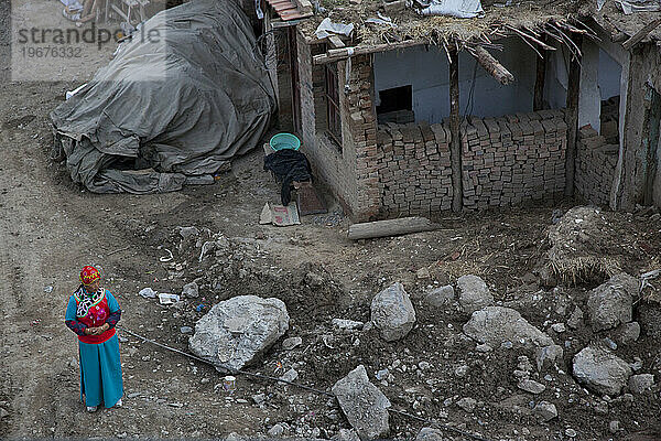 Junge tibetische Frau in traditioneller Kleidung steht neben einem im Bau befindlichen Haus in Xiahe  Gansu  China.