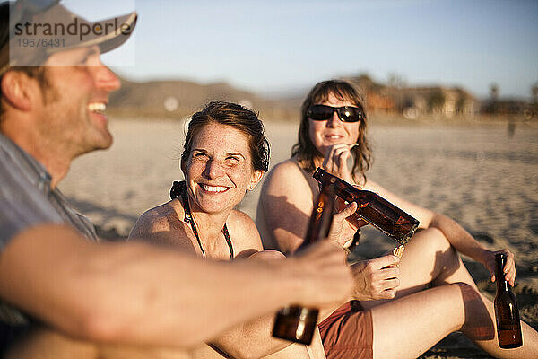Eine Gruppe Erwachsener hängt am Strand und genießt den Sonnenuntergang und ein paar kühle Biere.