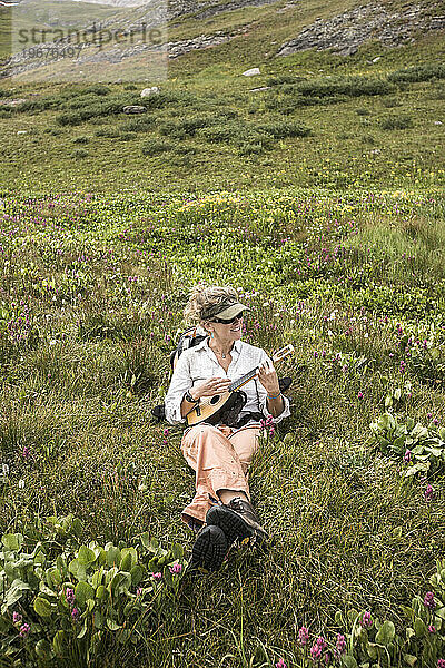 Eine Frau sitzt in einem Blumenfeld und spielt Ukulele.