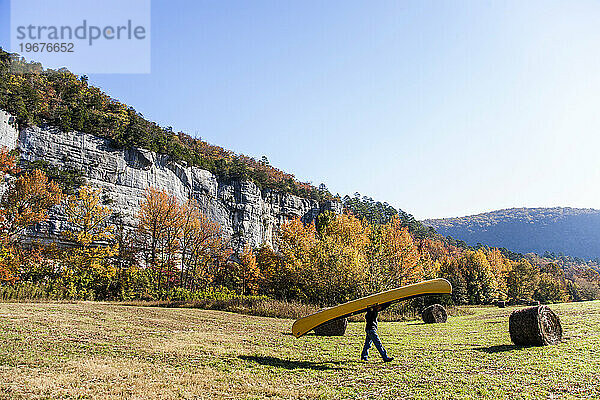 Ein Mann trägt sein gelbes Kanu durch ein Heufeld im ländlichen Arkansas.