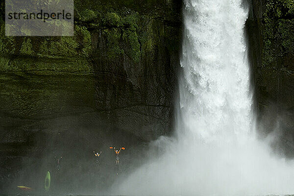 Drei Kajakfahrer feiern am Fuße eines sehr großen Wasserfalls.