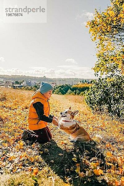 Ein Junge geht mit einem Corgi-Hund im Herbstwald spazieren