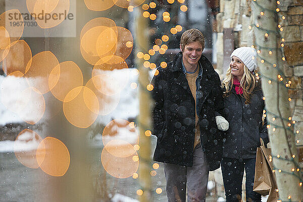 Junges attraktives Paar beim Einkaufen in einem Dorf bei fallendem Schnee.