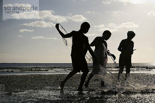 Eine Silhouette von drei jungen Erwachsenen  die das Netz einwickeln  nachdem sie bei Ebbe in der Nähe ihres Hauses gefischt haben.