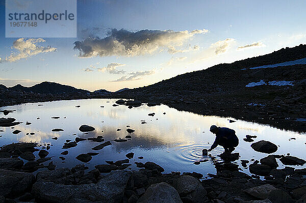 Die Silhouette eines Mannes  der Wasser aus einem kleinen Teich an der Sierra High Route  Kalifornien  sammelt.