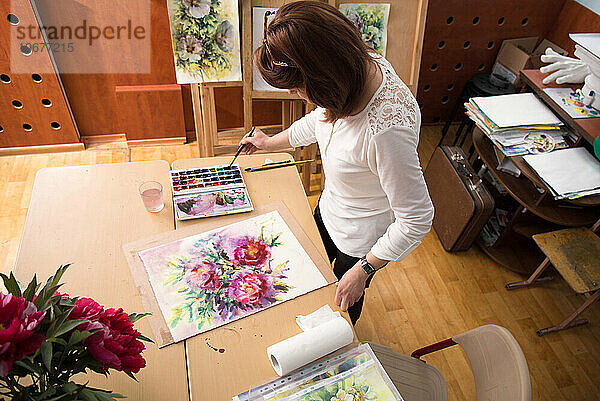 Die Künstlerin malt in ihrem Atelier einen Strauß Pfingstrosen  Draufsicht