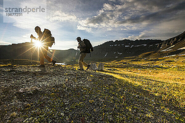 Zwei Menschen wandern bei Sonnenuntergang in den Bergen.