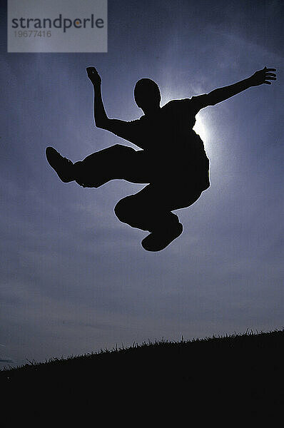 Die Silhouette eines jungen Mannes  der beim Spielen von Hacky Sack in die Luft springt  Ottawa  Ontario  Kanada.