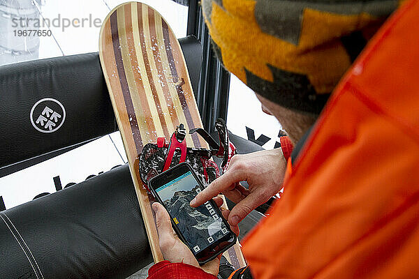 Snowboarder nutzt ein Telefon  um die Freeride-Linien im Lift zu überprüfen