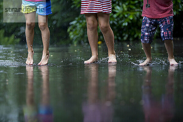 Drei kleine Kinder planschen im Regen
