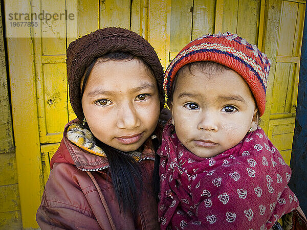 Ein junges nepalesisches Mädchen hält ein kleines Kind vor einer Tür in Nepal.