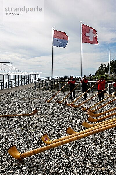 Eine Gruppe von Musikern spielt auf den Hörnern der Alpen mit der Flagge des Kantons Tessin und der Schweiz an einem sonnigen Tag in Monte Generoso  Tessin  Schweiz  Europa